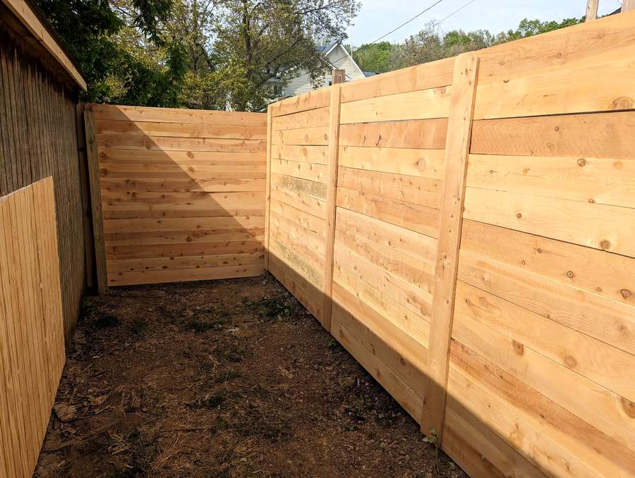 A horizontal cedar plank privacy fence wrapping the corner of a narrow side yard over bare soil.