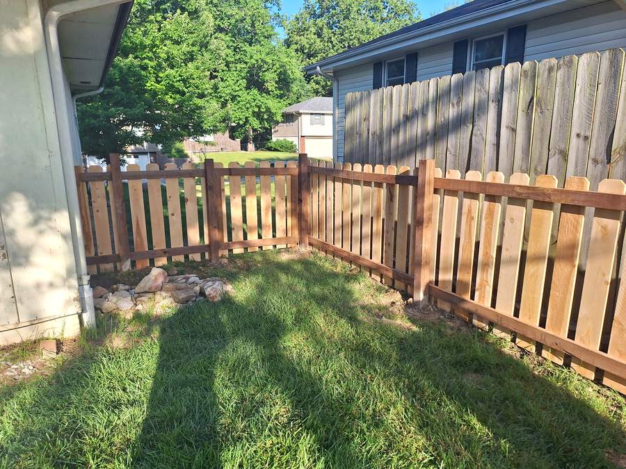 A cedar picket fence running along the side of a house out toward the property line.