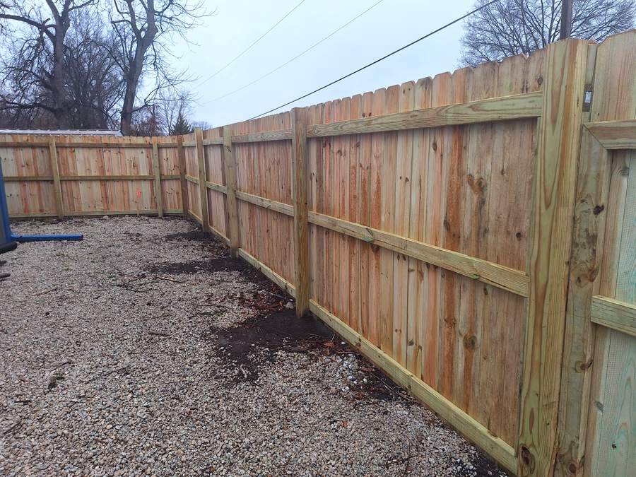 A solid cedar privacy fence enclosing a gravel parking pad beside a house.