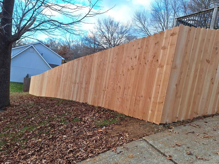 A solid cedar privacy fence stepping down a slope and ending square at a driveway.